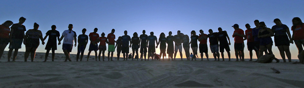 A line of people on a beach at sunrise