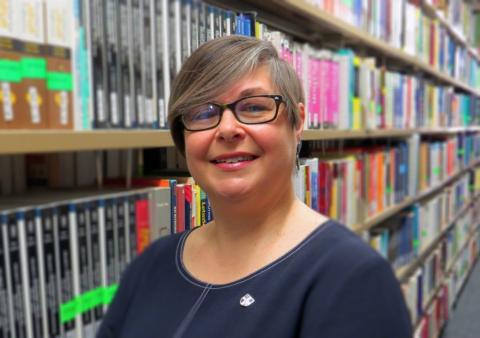 Photograph of Emma Walton standing by the bookshelves in Loughborough University Library